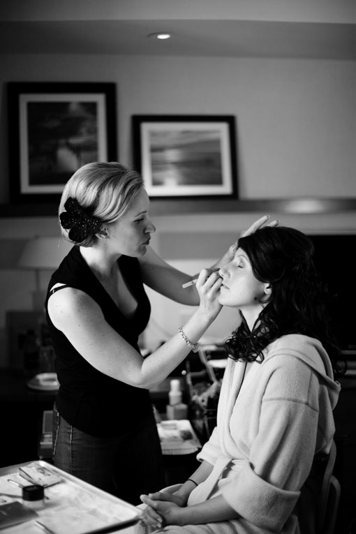 Bride receiving makeup application in black and white