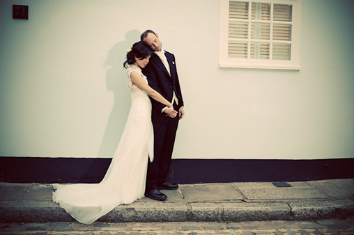 Newlyweds embrace against a building after their wedding