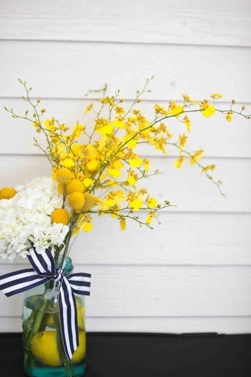 Yellow flower arrangement in a blue mason jar with lemons and ribbon