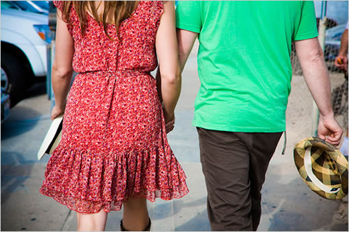 Couple walking hand in hand on a sunny day with a book and hat