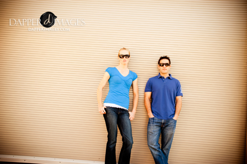 Couple in blue shirts and sunglasses standing against wall