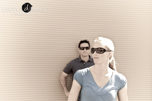 Couple wearing sunglasses posing casually against a wall backdrop