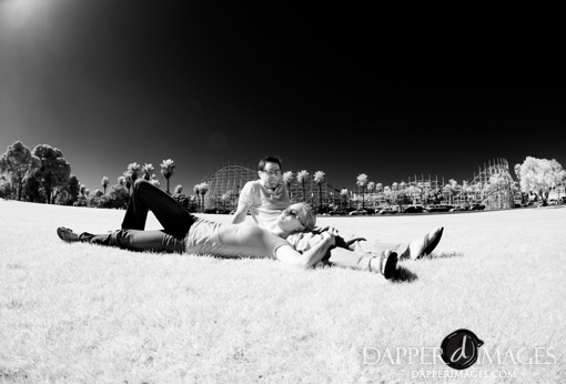 Couple relaxing on grass with roller coaster in background in monochrome