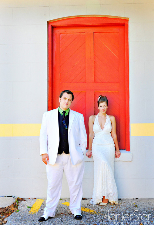 Wedding couple in white attire pose by a red door