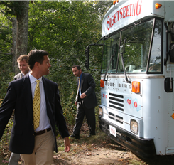 Three men in suits near a Blue Bird sightseeing bus in a forest