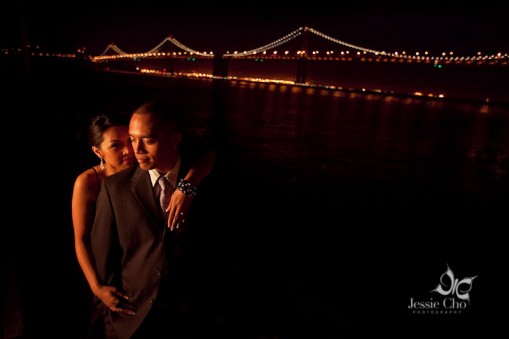 Couple embracing near a lit bridge at night, romantic photo