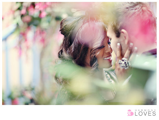 Smiling couple looking at each other surrounded by soft pink flowers