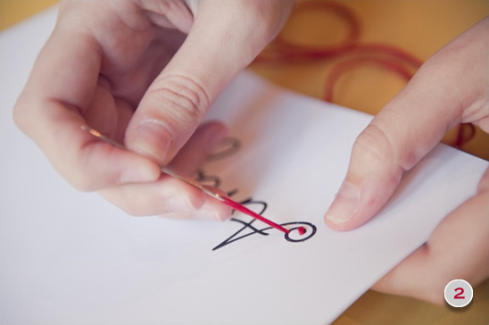 Hands embroidering a simple design with red thread