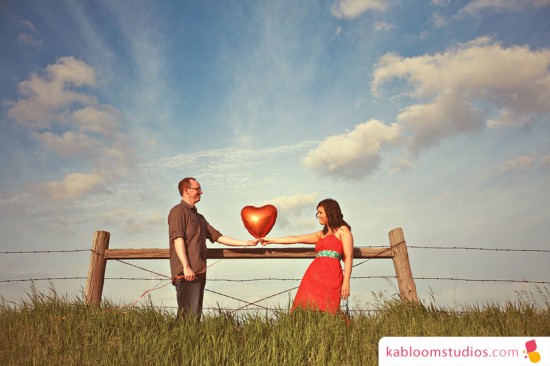 Couple holding a heart-shaped balloon in a field on a sunny day