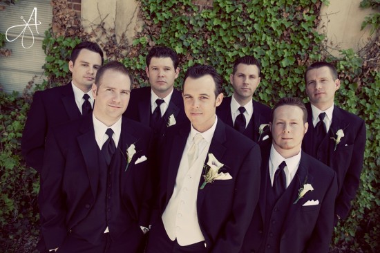 Groomsmen pose in black suits before the wedding ceremony