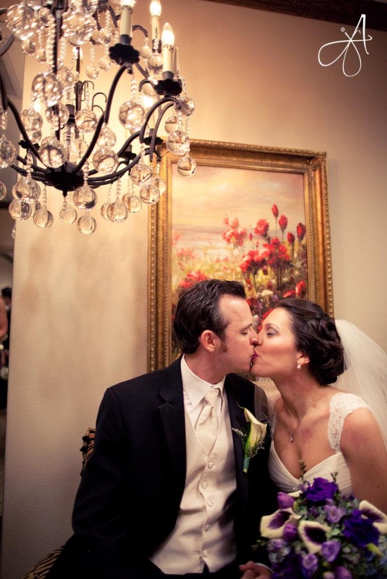 Newlyweds share a kiss beneath a chandelier at their wedding