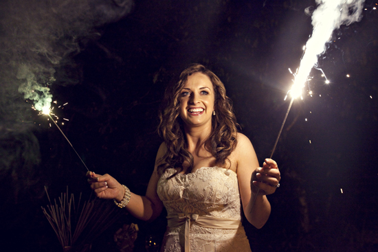 Happy bride holds sparklers, smiling brightly at a night wedding