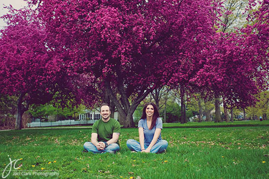 Couple sits under a vibrant pink flowering tree in a park