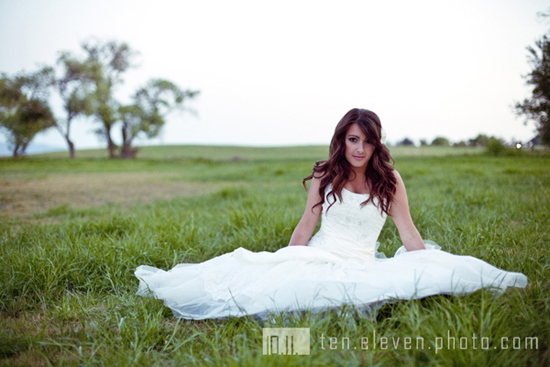Bride in a wedding dress sitting in a lush green field smiling