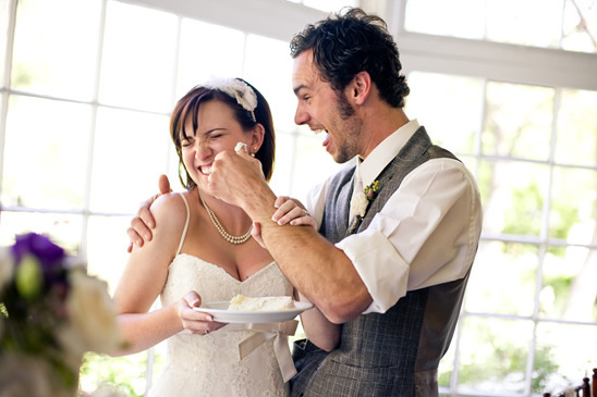 Groom smearing cake on bride's face at a joyful wedding reception