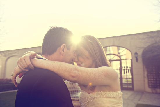 Couple embrace on wedding day with the sun shining behind them