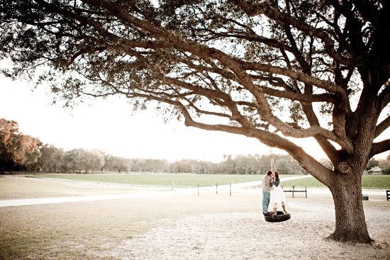 Couple kissing on tire swing under a large tree