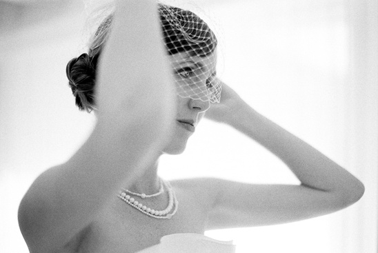 Elegant bride adjusting veil, wearing pearls in black and white