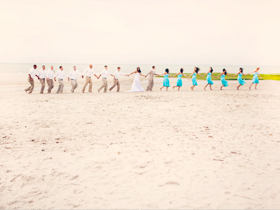 Beach wedding party holding hands, bride in white