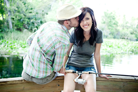 Happy couple enjoying a kiss by the lake with a fishing rod