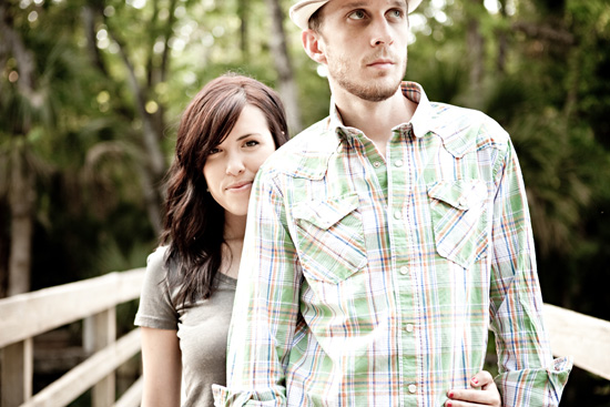 Couple posing romantically outdoors on a wooden bridge, smiling