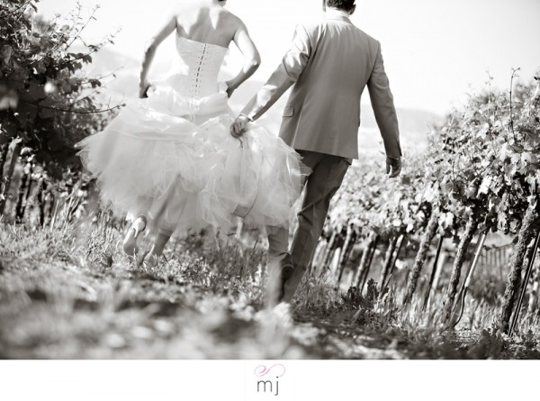 Bride and groom joyfully run through vineyard