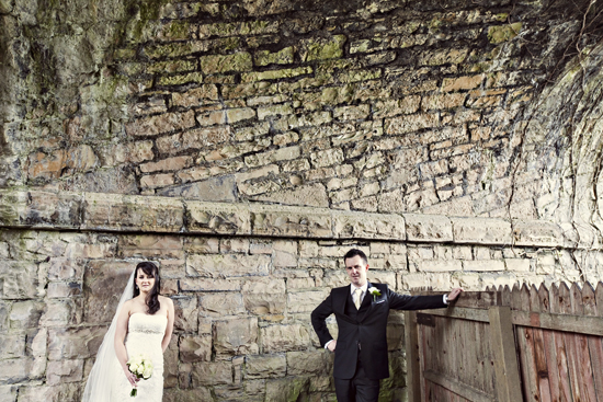Bride and groom pose by old stone wall
