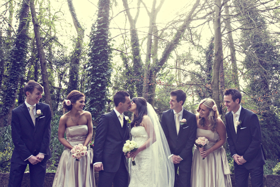Happy wedding couple kissing, surrounded by bridesmaids and groomsmen in a forest