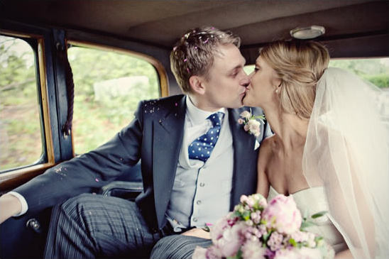 Newlyweds sharing a first kiss in vintage wedding car