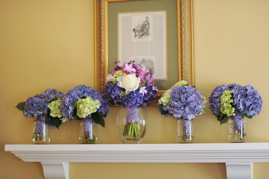 Beautiful hydrangea bouquets arranged on a white shelf below framed art
