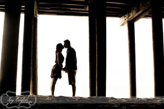 Couple kissing under pier, romantic silhouette