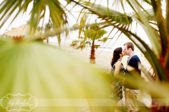 Couple kissing, framed by palm leaves, romantic beach scene