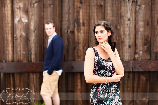 Woman in floral dress looks away from man near wooden fence