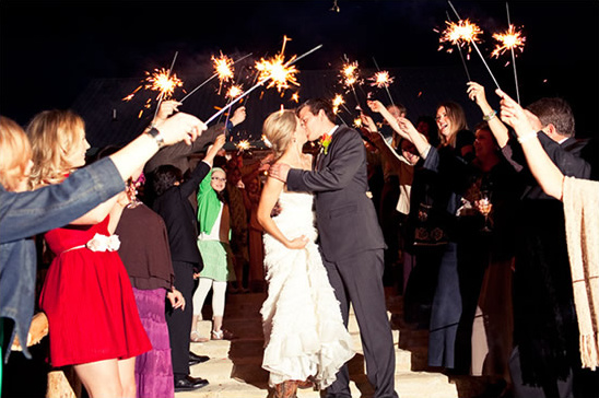 Wedding sparkler send-off with the happy couple kissing surrounded by guests
