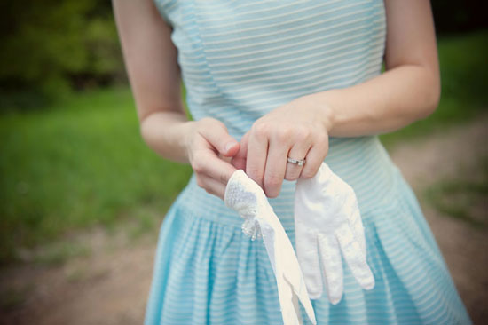 Woman holding white gloves in a light blue dress with a ring