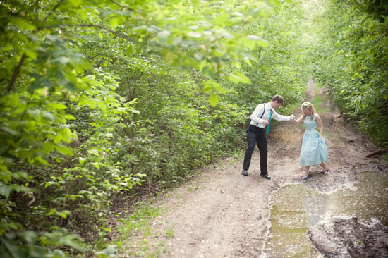 Couple helping each other walk across muddy forest path