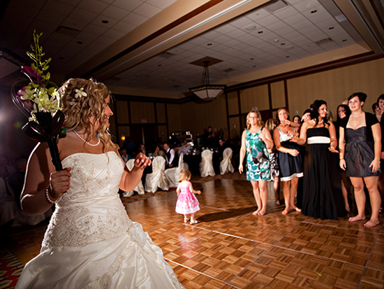 Bride tossing bouquet to group of women at wedding reception