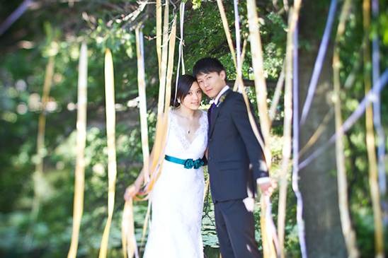Asian couple in wedding attire pose outdoors with ribbons