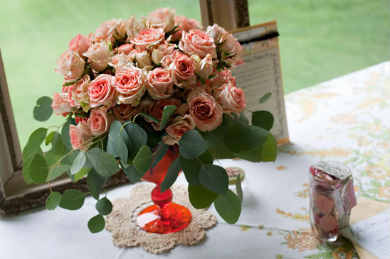 Pink roses with eucalyptus in a red glass vase on a table