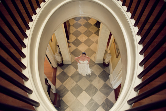 Bride stands on checkered floor viewed from above stairs