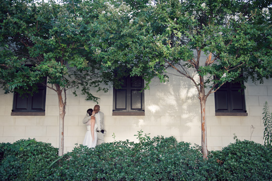 Bride and groom embrace near trees and window