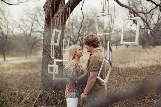 Couple gazing at each other under picture frames hanging from a tree