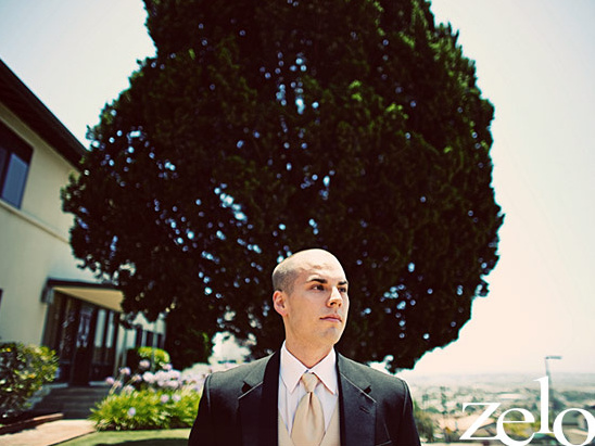 Man in a suit standing in front of a large tree during the day