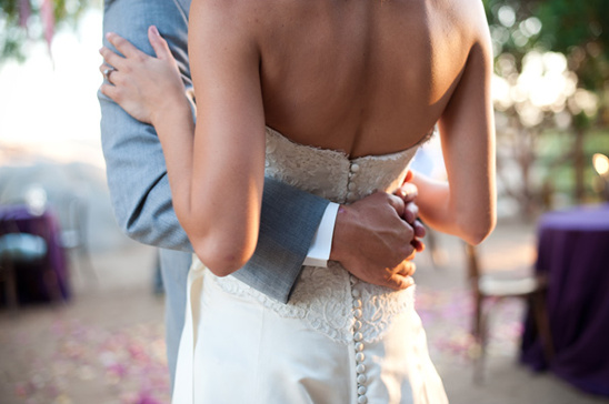 Bride and groom embrace, wedding dress detail