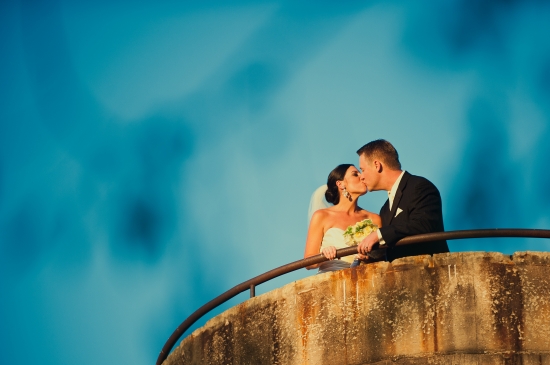 Newlyweds share a kiss on a balcony overlooking a beautiful sky
