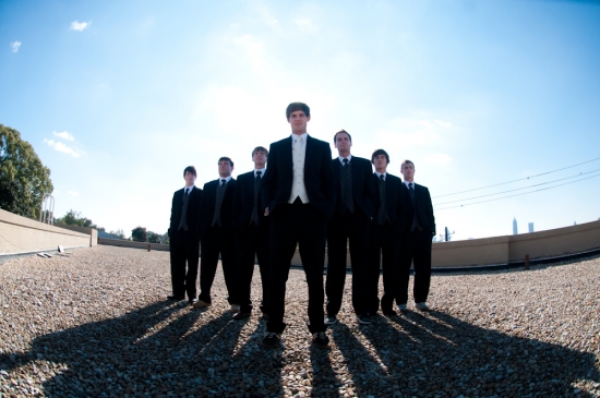 Men in black suits standing on a rooftop on a sunny day