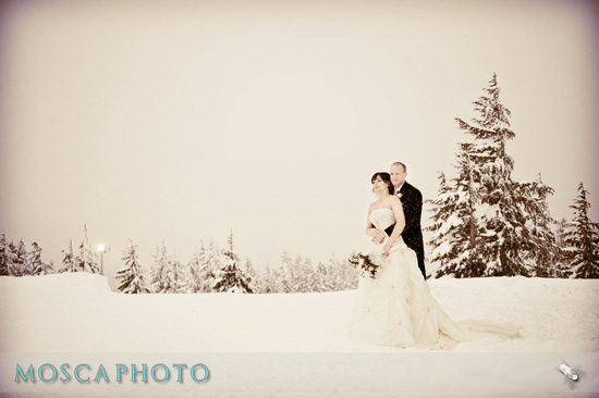 Winter wedding couple posing in the snow by evergreen trees