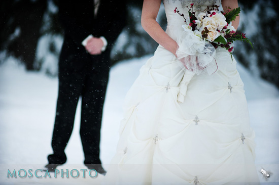 Bride in elegant dress holds bouquet with groom in the background