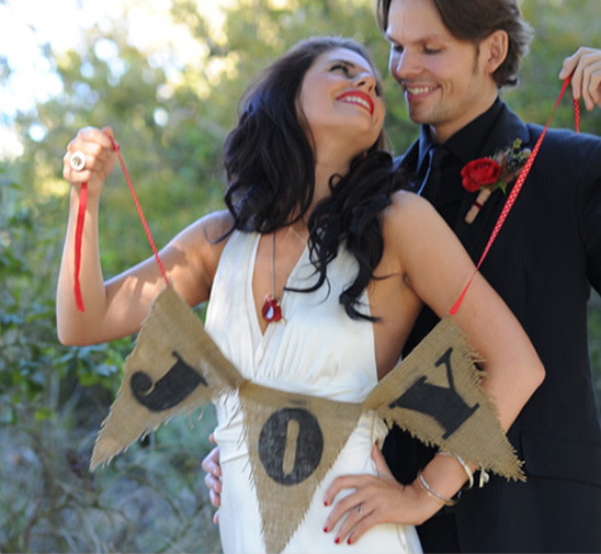 Happy couple holding burlap JOY banner at wedding