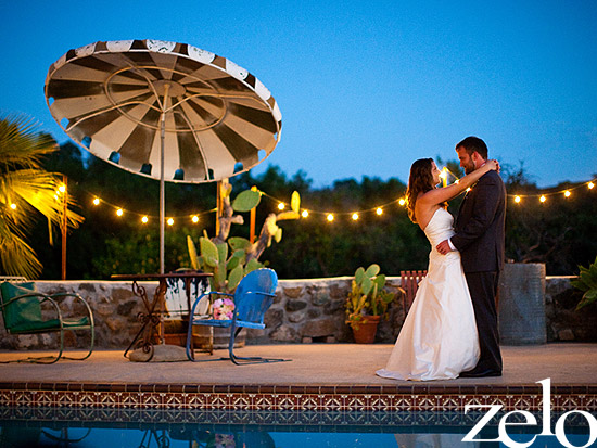 Bride and groom dance under market lights by the pool